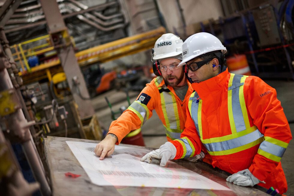 Two Metso workers in PPE pointing at a paper