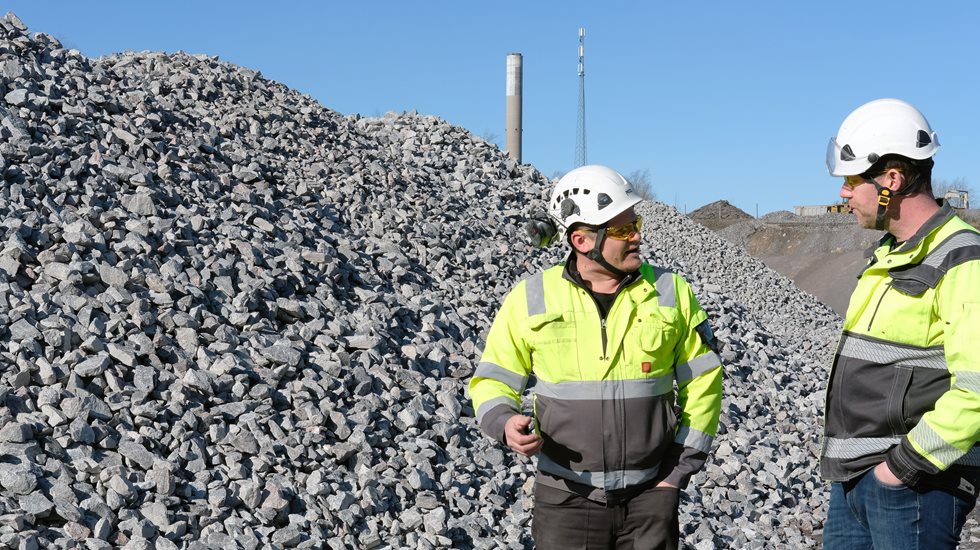 Two people standing in front of piles of aggregate. 