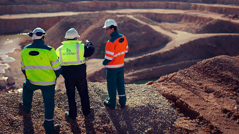 Three men standing on the edge of a quarry and talking.