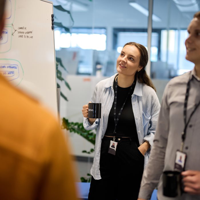 Three employees smiling and looking at a whiteboard.