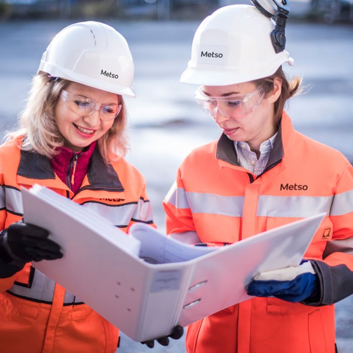 Two women with work gear looking at folder in their hands.