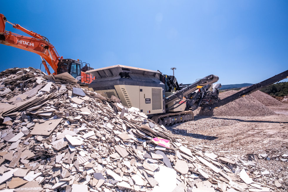 El triturador de impacto móvil Metso Nordtrack I908S con pantalla integrada está triturando y cribando eficazmente el excedente de residuos de azulejos cerámicos para ser reutilizados en el proceso de fabricación de azulejos.