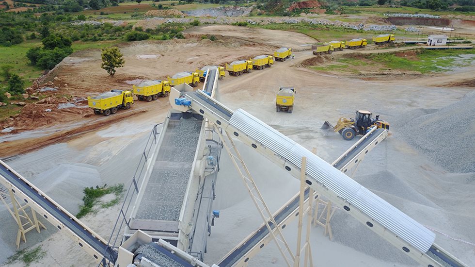 A screening equipment being fed in a quarry with haul trucks at the back.