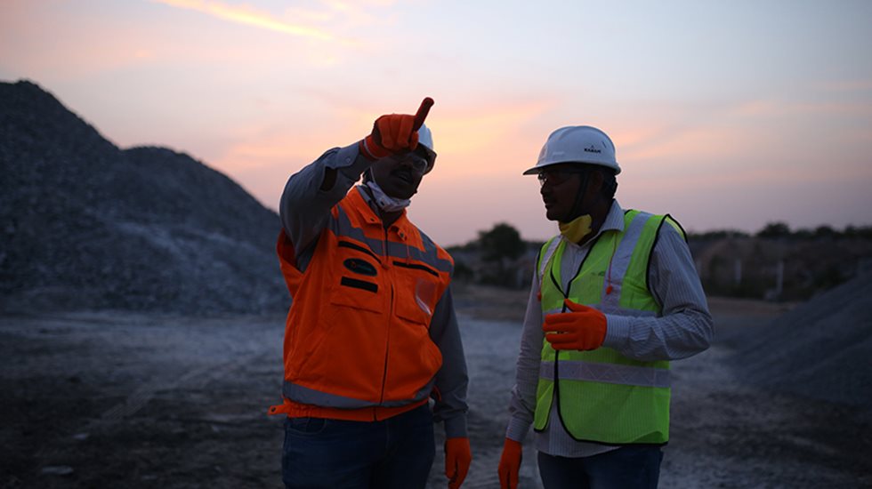 Two men in a sunset at a quarry facing the camera and the other pointing forward.